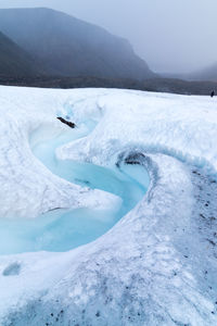 Milky blue meltwater running from longyearbyen glacier in svalbard. strong snowfall and cloudy sky