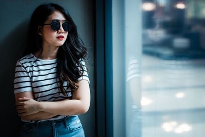 Young woman wearing sunglasses standing by window