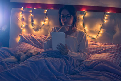 Young woman using digital tablet while sitting on bed at home