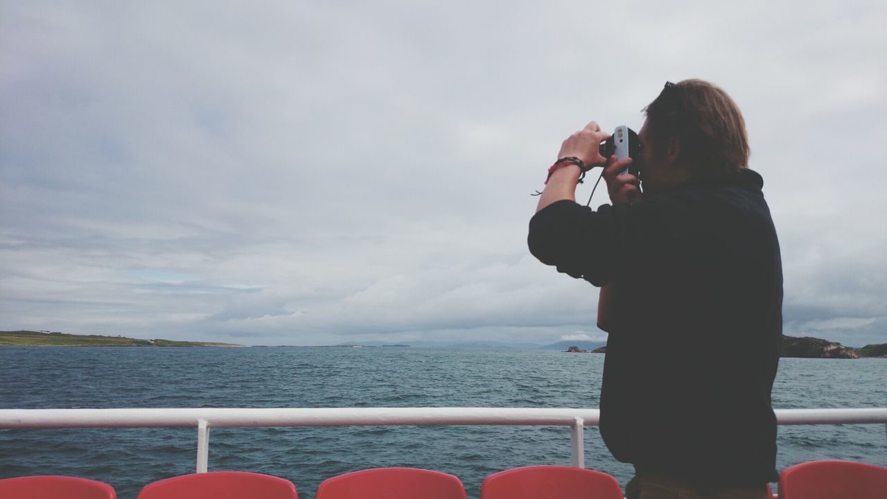 water, sky, sea, lifestyles, rear view, leisure activity, cloud - sky, standing, railing, looking at view, sitting, men, nature, three quarter length, cloudy, scenics, waist up, cloud