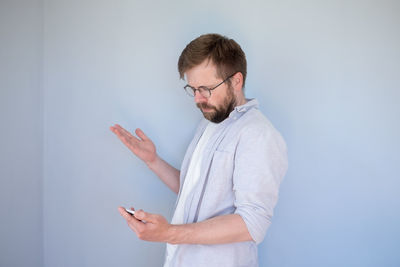 Young man using mobile phone against wall