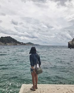 Rear view of mature woman standing by sea against cloudy sky