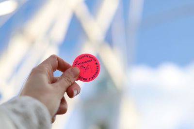 Cropped hand holding red token against sky