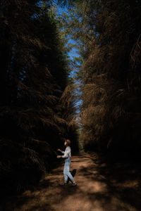 Full length side view of woman standing amidst trees in forest