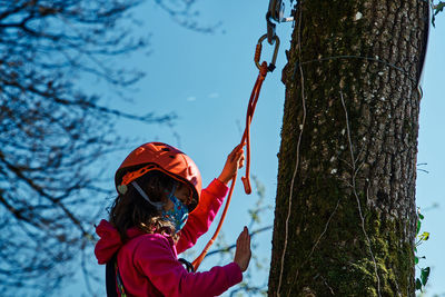 Little girl with protections practicing climbing between trees with ropes and nets