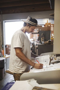 Side view of carpenter writing on document in workshop