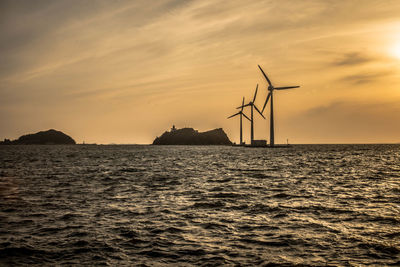 Traditional windmill by sea against sky during sunset