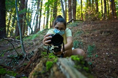 A teenage girl records a video on a fallen tree in the forest