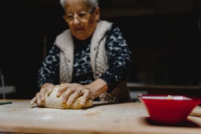 Senior female standing at table in cozy kitchen and kneading raw dough while preparing pastry for cooking domestic italian tortellini