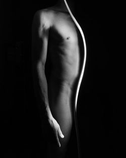 Midsection of naked man standing against black background