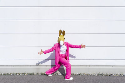 Low angle view of woman with pink umbrella standing against wall