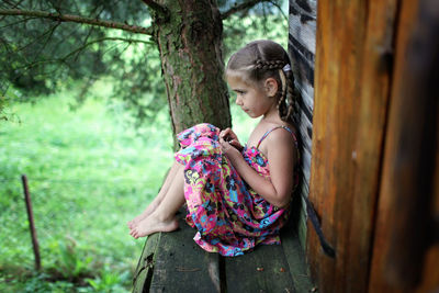 Girl looking away while sitting on tree trunk in forest