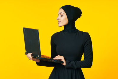 Young woman looking away while standing against yellow background