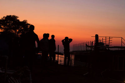 Silhouette people standing by railing against sky during sunset