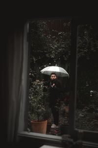 Woman standing by wet window in rainy season