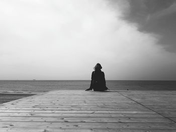 Rear view of woman sitting on pier over sea against sky