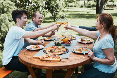 Friends making toast during summer picnic outdoor dinner in a home garden