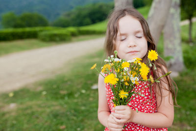 Cute girl holding yellow flowers while standing on grass