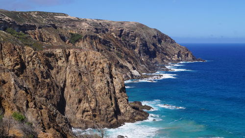 Scenic view of cliff by sea against clear sky