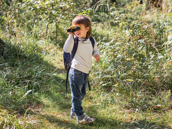 Curious boy with binoculars on hike in forest. outdoor leisure activity for kids. sunny day summer.