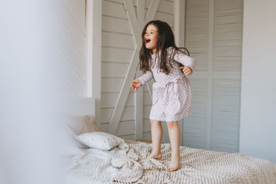 Cute long hair little girl jumping on parents bed at bright room, scandinavian interior