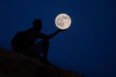 Optical illusion of man holding full moon in clear blue sky