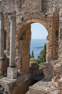 Columns and arch at old ruins of ancient greek theater with sea in background