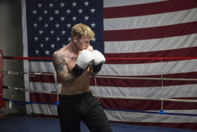 Shirtless boxer practicing in boxing ring against american flag