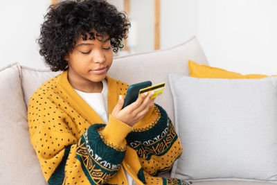 Young woman using mobile phone while sitting on sofa at home