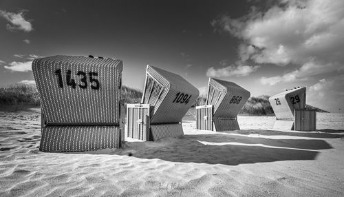 Hooded chairs on beach against sky