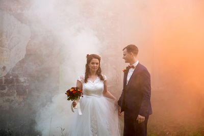 Full length of newlywed couple standing by abandoned built structure