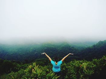 High angle view of young woman with arms outstretched standing on mountain during foggy weather