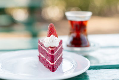 Piece of red velvet cake decorated with fresh berries in a white plate on the table, a cup of