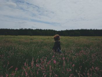 Rear view of girl standing on field against sky