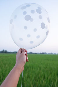 Cropped hand holding white helium balloon by farm
