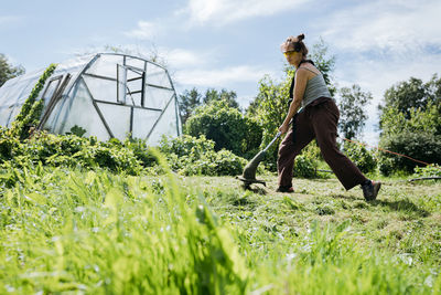 Woman cutting grass with a trimmer and a greenhouse in. the background