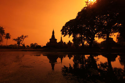 Reflection of silhouette trees in lake against orange sky