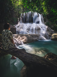 Solo traveler relax and looking at scenic waterfall in forest. erawan fall, kanchanaburi, thailand.