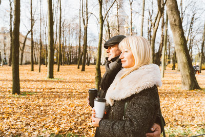 Mature couple holding disposable coffee cup while standing at park during autumn