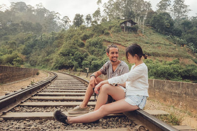 Young man sitting on railroad track by trees