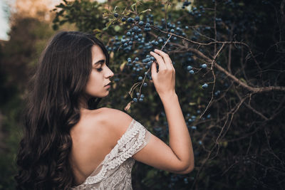 Young woman looking away while standing against tree