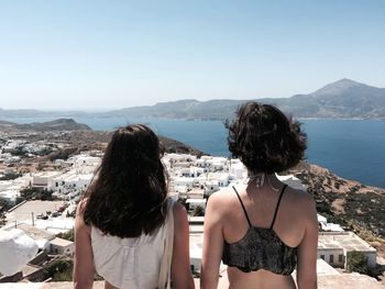 Rear view of women looking at river and mountains against clear sky