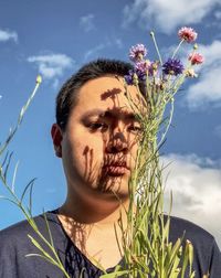 Close-up of young man with cornflowers against cloudy blue sky.