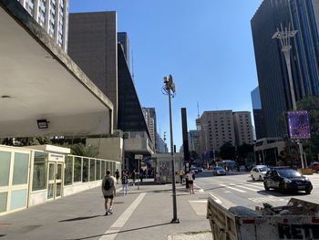 People walking on road by buildings against sky in city
