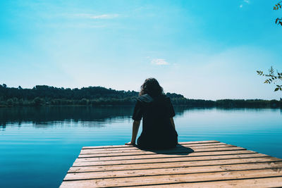 Rear view of woman sitting on pier over lake against sky