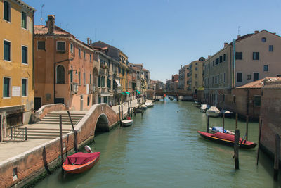 Boats moored in canal amidst buildings in city against clear sky