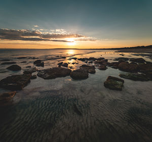 Wide angle long exposure shot of textured sand and rock formation on beach during sunset