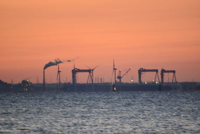 Commercial dock by sea against orange sky