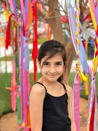 Portrait of smiling girl standing by colorful ribbons hanging from branches