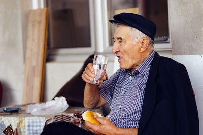 Senior man having food and drink while sitting on seat